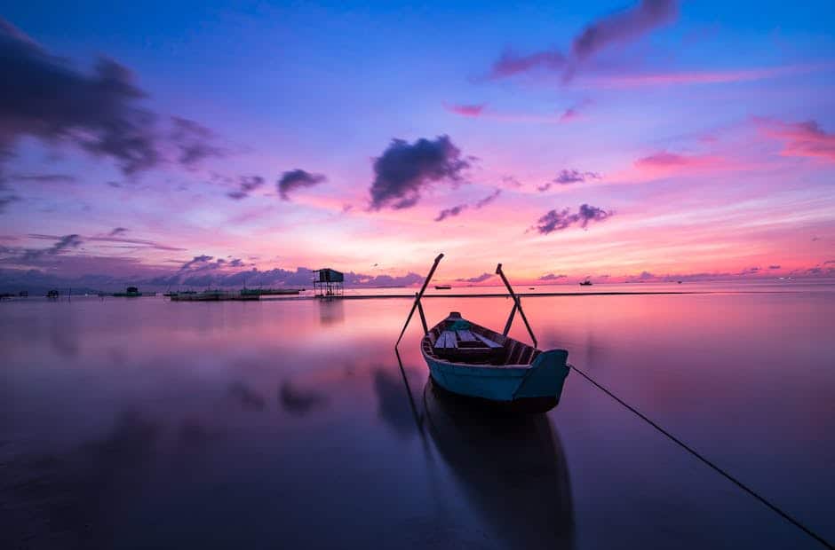 A tranquil tropical sunrise with a lone boat on calm waters.