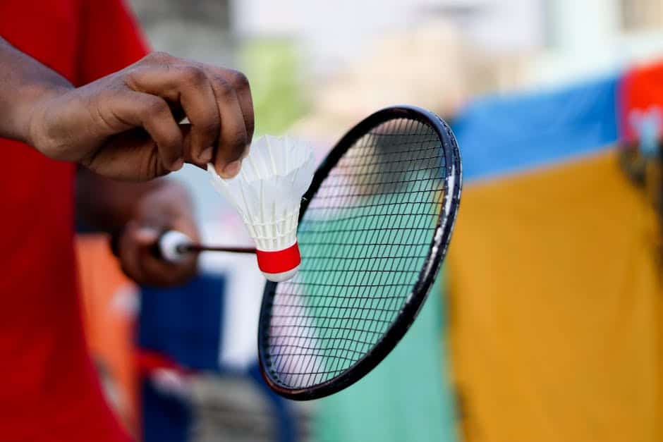 Close-up of a hand holding a shuttlecock and badminton racket, ready to serve.