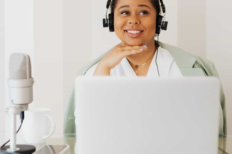 A woman smiling while podcasting at home, wearing headphones and using a microphone.