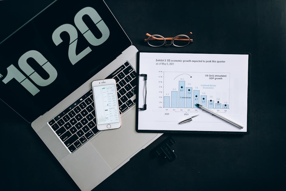 Top view of financial analysis tools on a desk including a laptop, smartphone, and graphs.