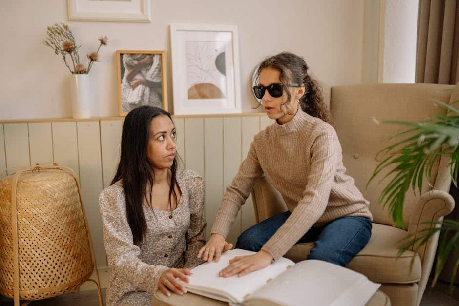 Two women reading a Braille book inside a cozy room, fostering educational connection.