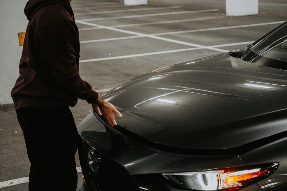 A person opens the car hood in a dimly lit parking garage, showcasing urban transportation.
