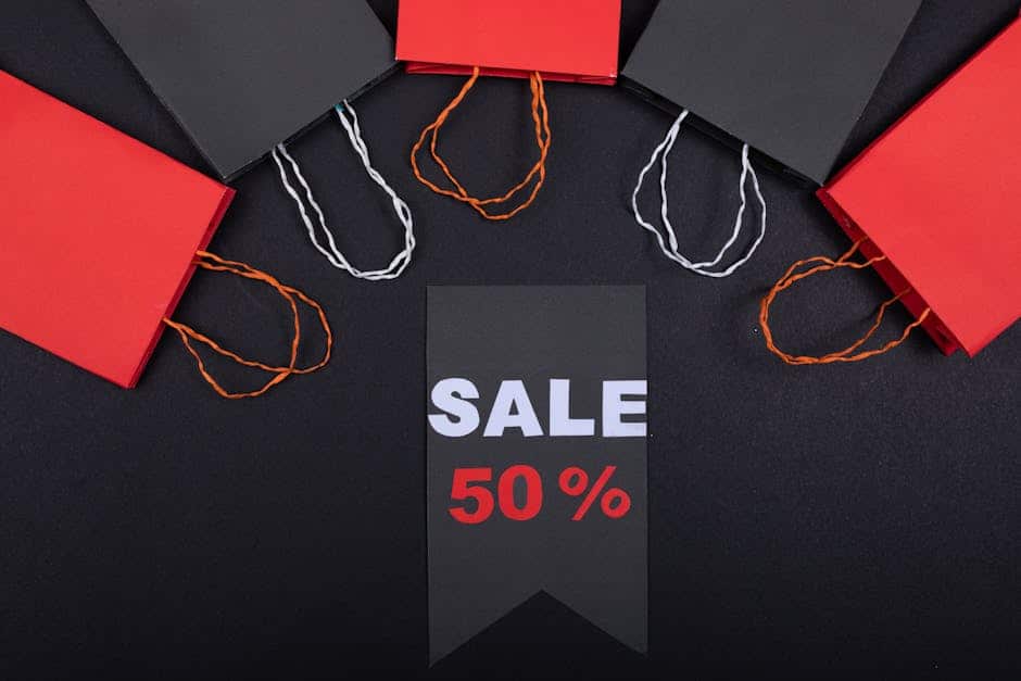 Flat lay of black and red shopping bags surrounding a sale sign with 50% discount on black background.