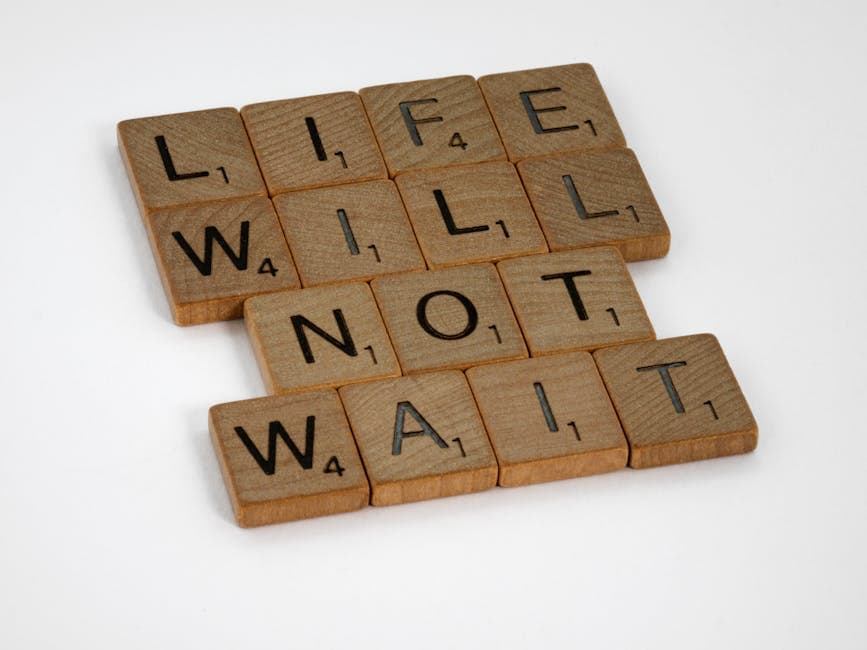 Wooden Scrabble tiles spelling 'Life Will Not Wait' on a white background.