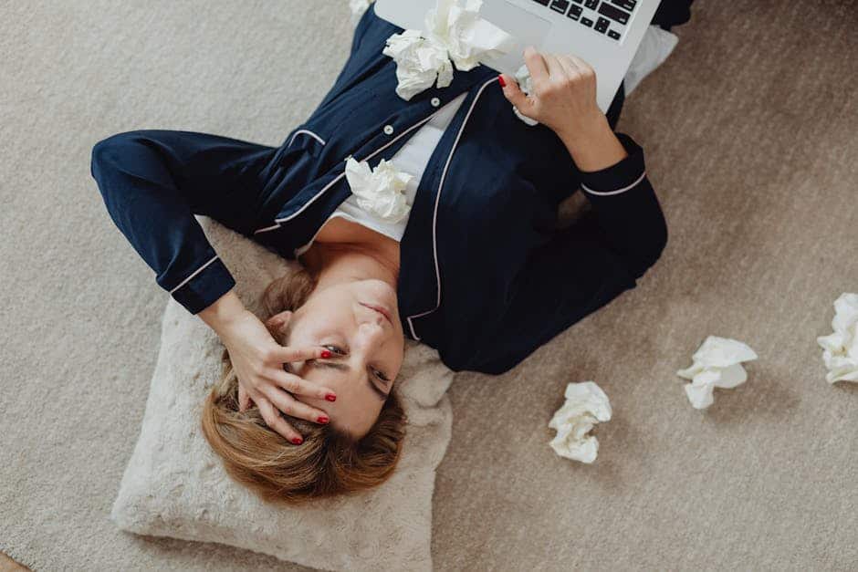 A woman in pajamas, stressed and lying on the floor with a laptop and scattered tissues.