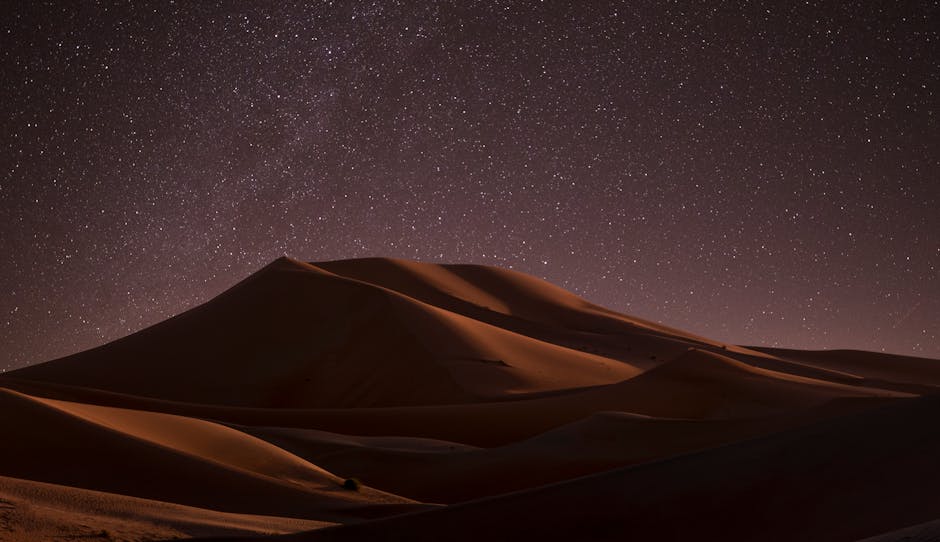 A captivating view of starlit sky above serene desert dunes at night, offering a tranquil escape.