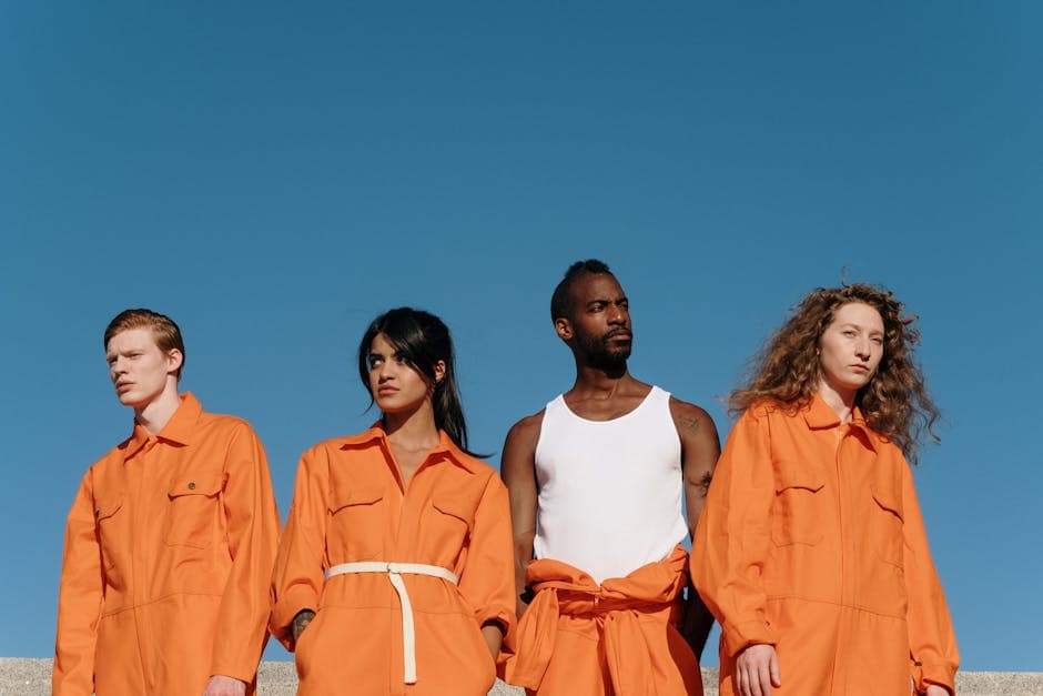 Four adults in vibrant orange uniforms standing outdoors against a clear blue sky.