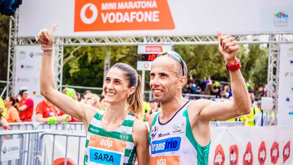 Two athletes celebrate their marathon achievement with thumbs up at the finish line.