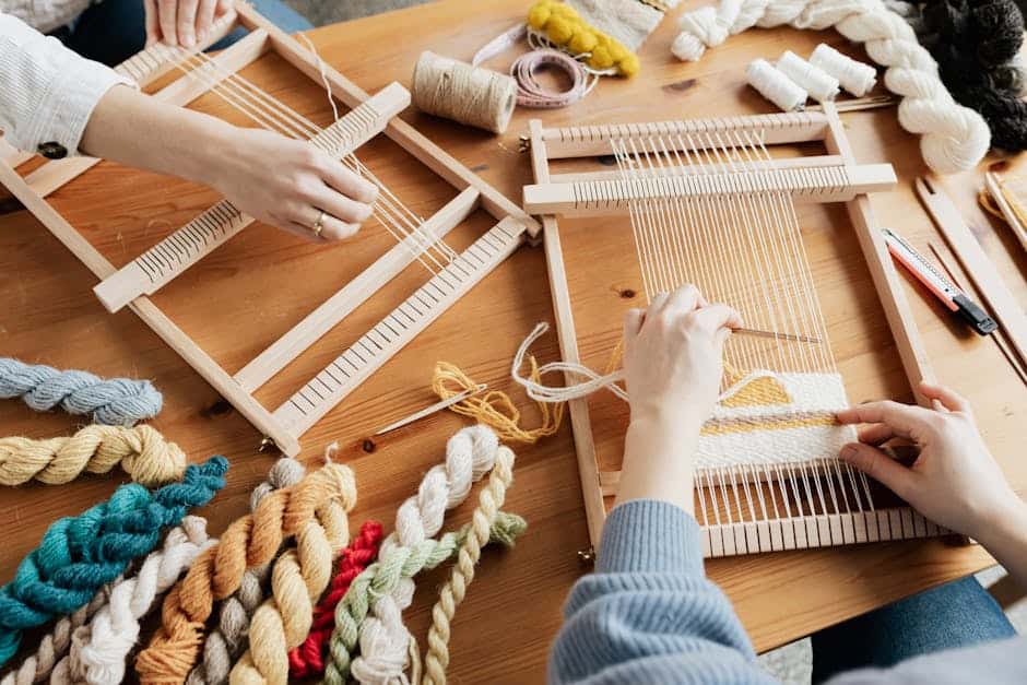Two people weaving on wooden looms with colorful yarns in a workshop setting.