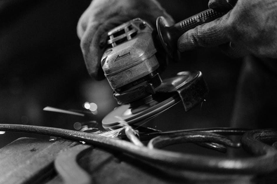 Black and white close-up of an angle grinder creating sparks on metal, showcasing craftsmanship.