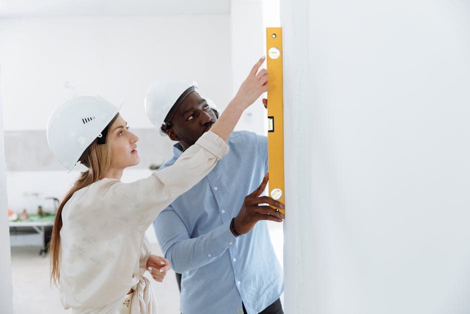 Two construction workers using a level tool on an indoor wall for accuracy.