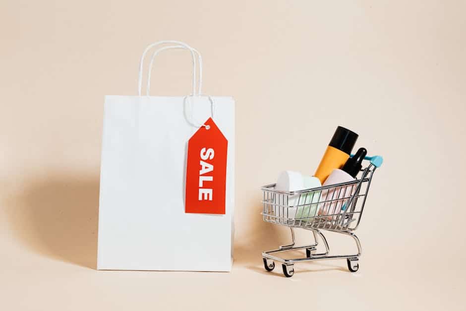White shopping bag with red sale tag and mini shopping cart on beige background.
