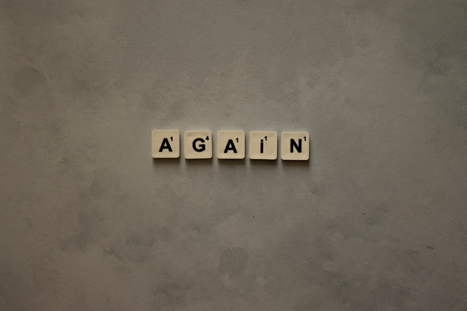 Close-up of Scrabble tiles spelling out 'Again' on a textured background.