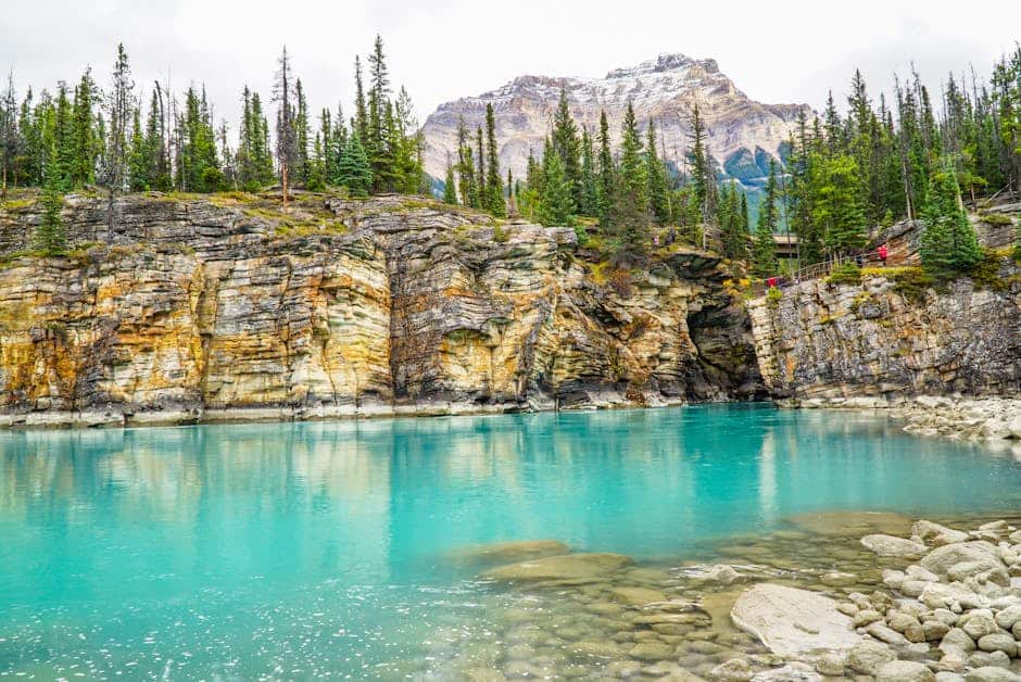 Vibrant turquoise waters of Maligne Canyon in Jasper National Park, surrounded by rocky cliffs and pine trees.